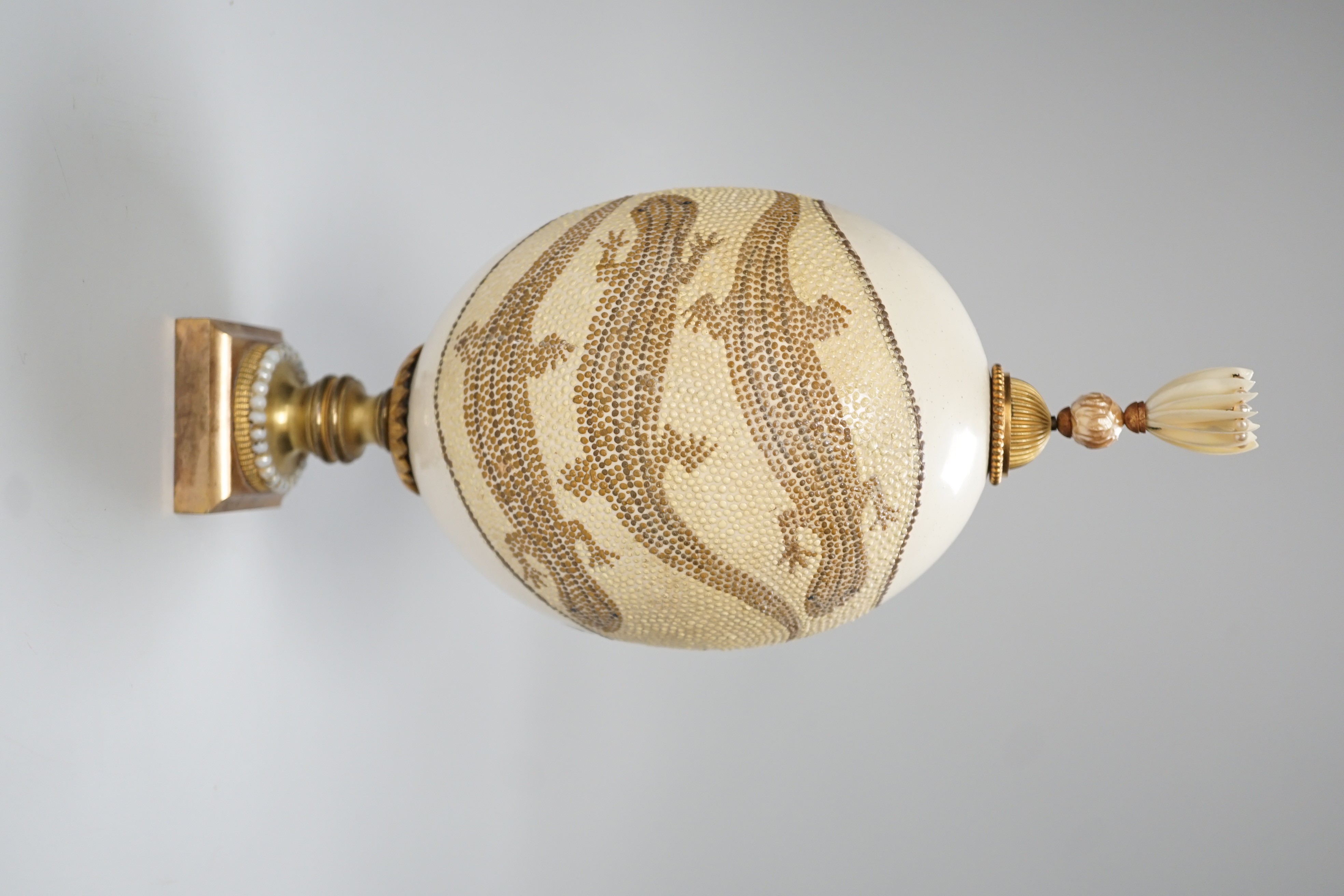 A decorated ostrich egg on gilt stand with a gilt and seed finial, 27cms high